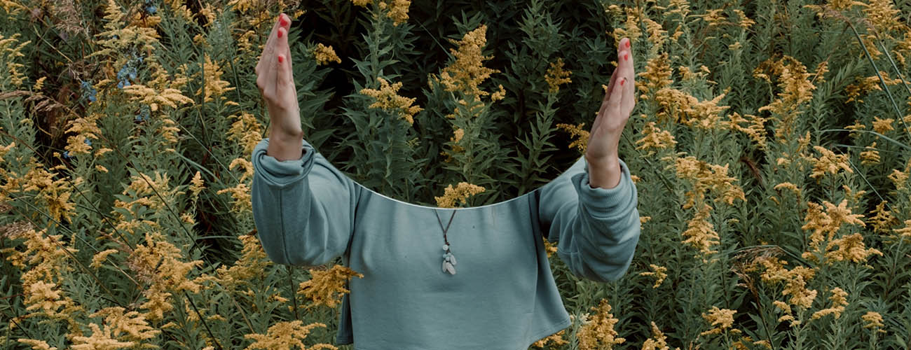 femme tenant un minoir devant elle dans un champs de plantes vertes et jaunes