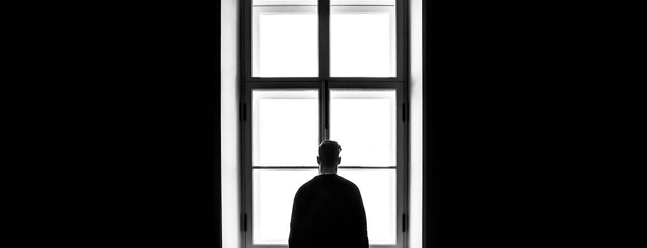 jeune homme de dos face à une fenêtre haute, photo en noir et blanc